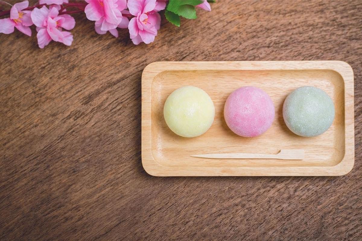 Three colorful mochi (yellow, pink, green) on wooden tray with pink cherry blossoms