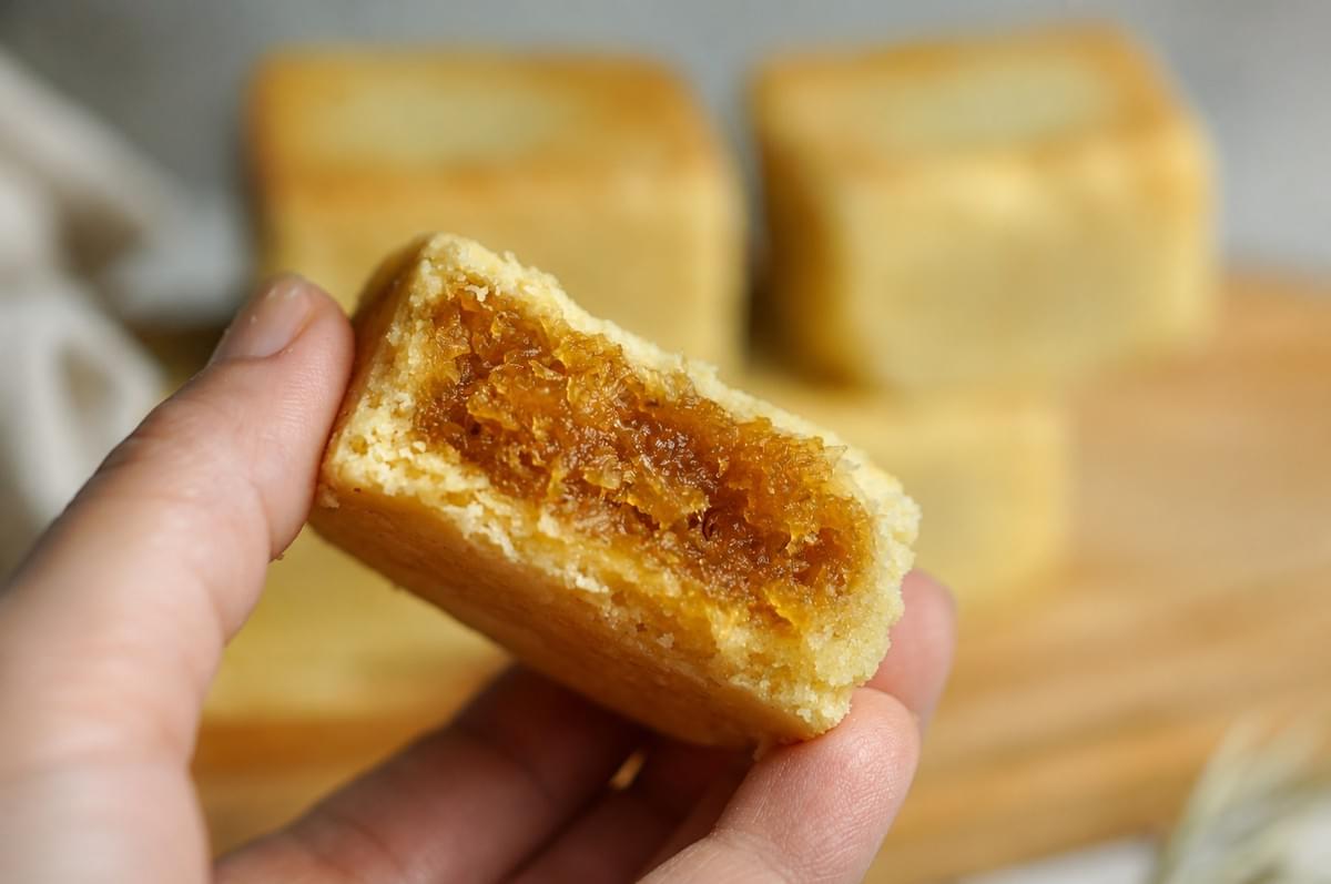 A hand holding a halved Taiwanese pineapple cake, showcasing its rich fruit jam center.