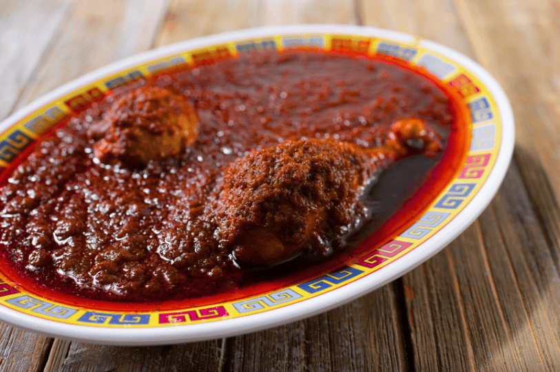 A chicken drumstick and hard-boiled egg smothered in a dark, thick Doro Wat sauce, served on a decorative white platter with a yellow and blue rim.