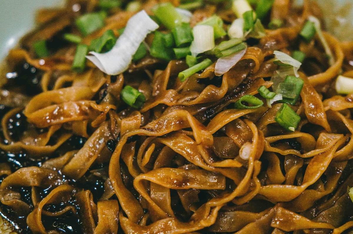 Close-up of savory Mee Pok noodles tossed in dark soy sauce and garnished with freshly chopped green onions.