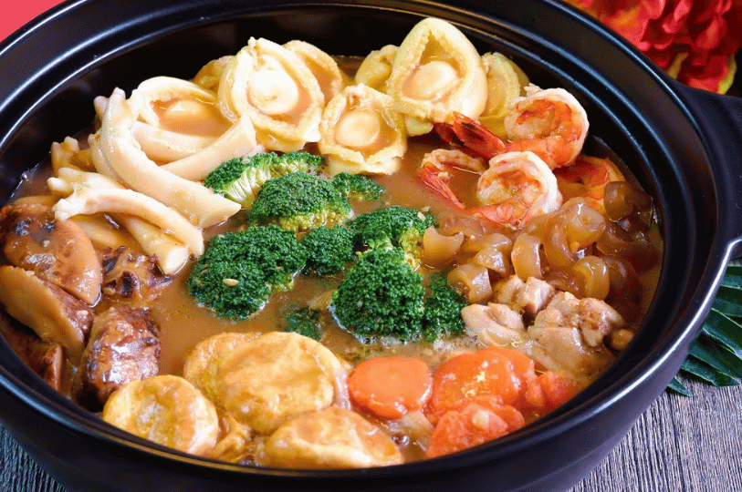 A vibrant pot of Pen Cai showing a variety of textures including fish maw, sea cucumber, prawns, and scallops simmering in a golden broth.