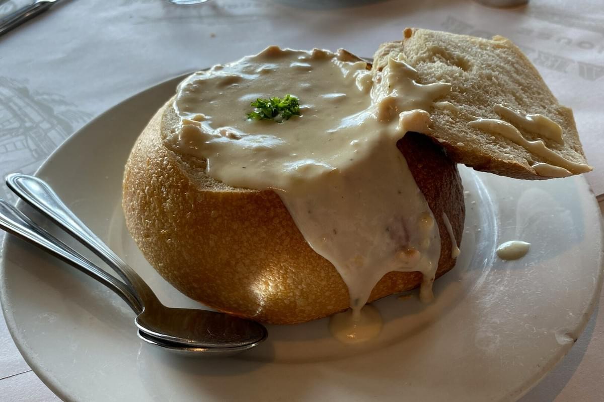 A bowl of New England clam chowder with a spoon on a white plate, a creamy seafood dish for landlocked expats