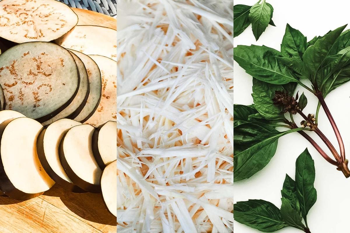 Sliced eggplant, shredded bamboo shoots, and fresh Thai basil leaves arranged side by side as ingredients for Thai cooking.