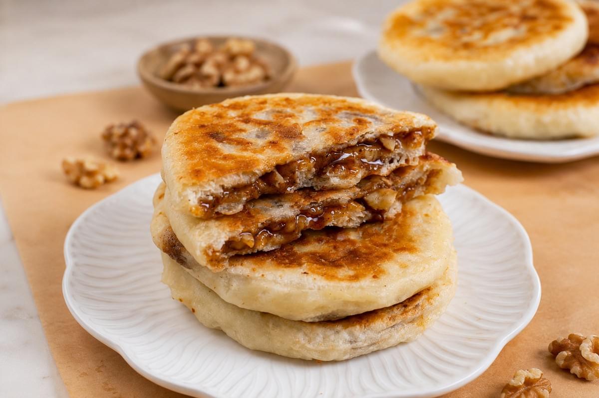 Stack of warm hotteok pancakes on a plate, cut open to reveal a sticky brown sugar and walnut filling.