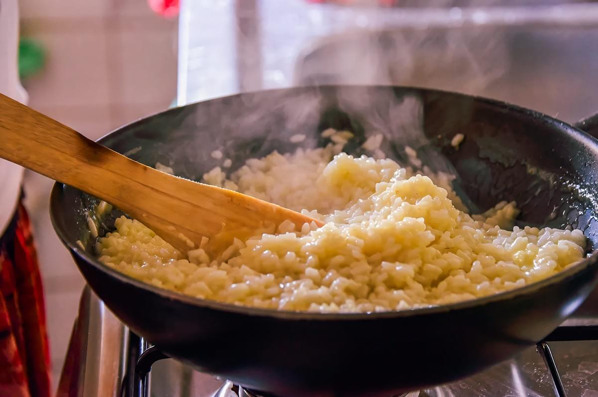 Creamy risotto being stirred in a hot pan with a wooden spatula as steam rises during cooking.