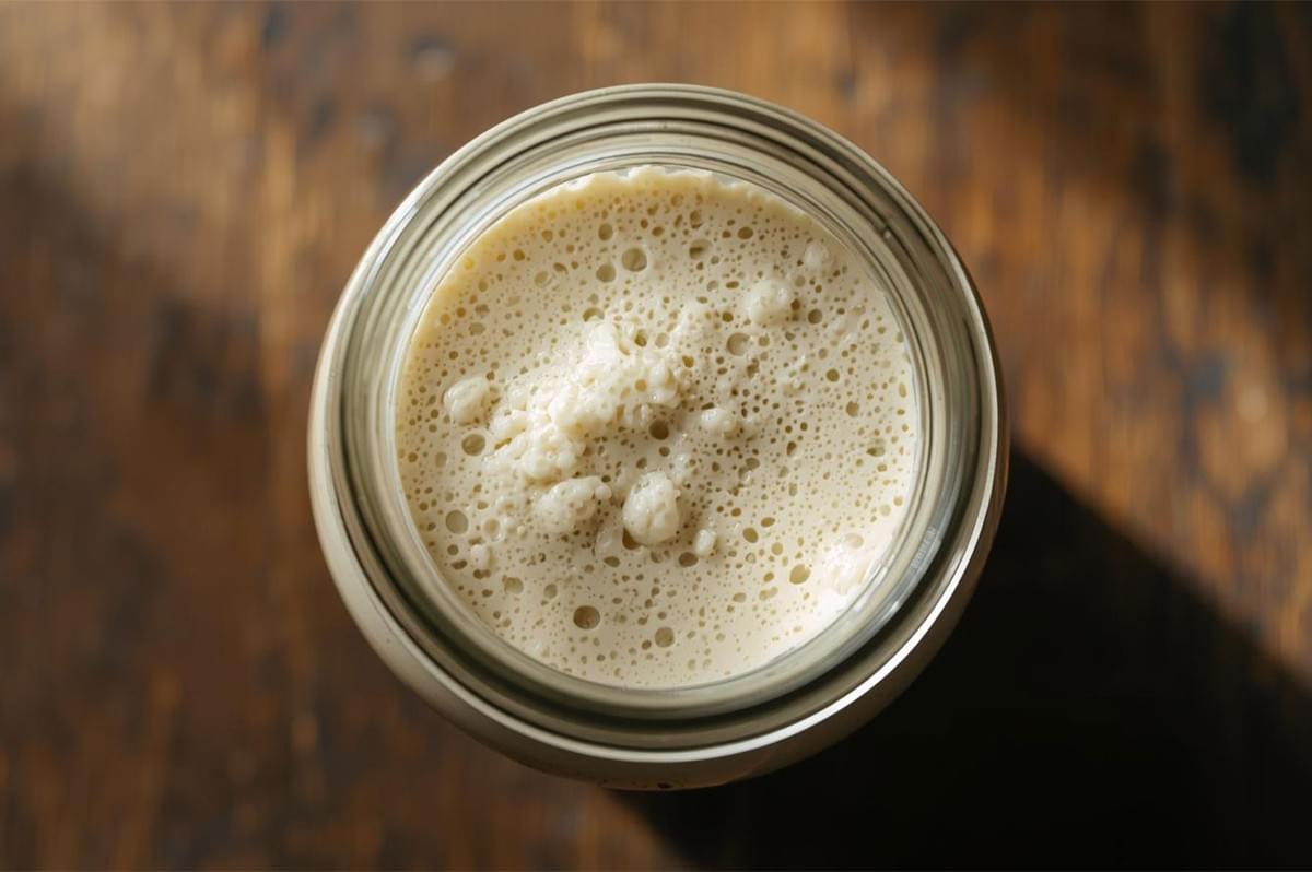 An overhead shot looking down into a glass jar filled with a perfectly active, bubbly sourdough starter, showing a porous, foamy surface ready for baking.