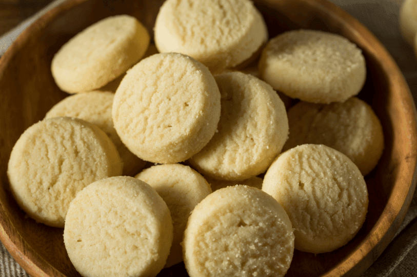 A cluster of round, thick-cut shortbread cookies piled in a wooden bowl, emphasizing their uniform light-gold bake and rustic, homemade appearance.