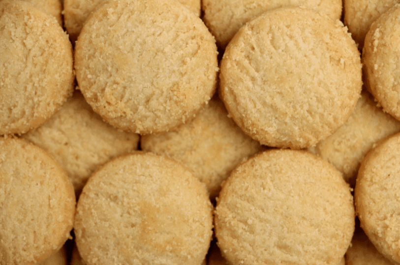 A top-down, full-frame view of several round shortbread cookies packed closely together, showing a consistent sandy texture and delicate ridged patterns on top.