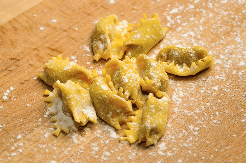 Freshly crafted stuffed pasta with jagged edges, resembling Piedmontese agnolotti del plin, lightly dusted with flour on a wooden cutting board.