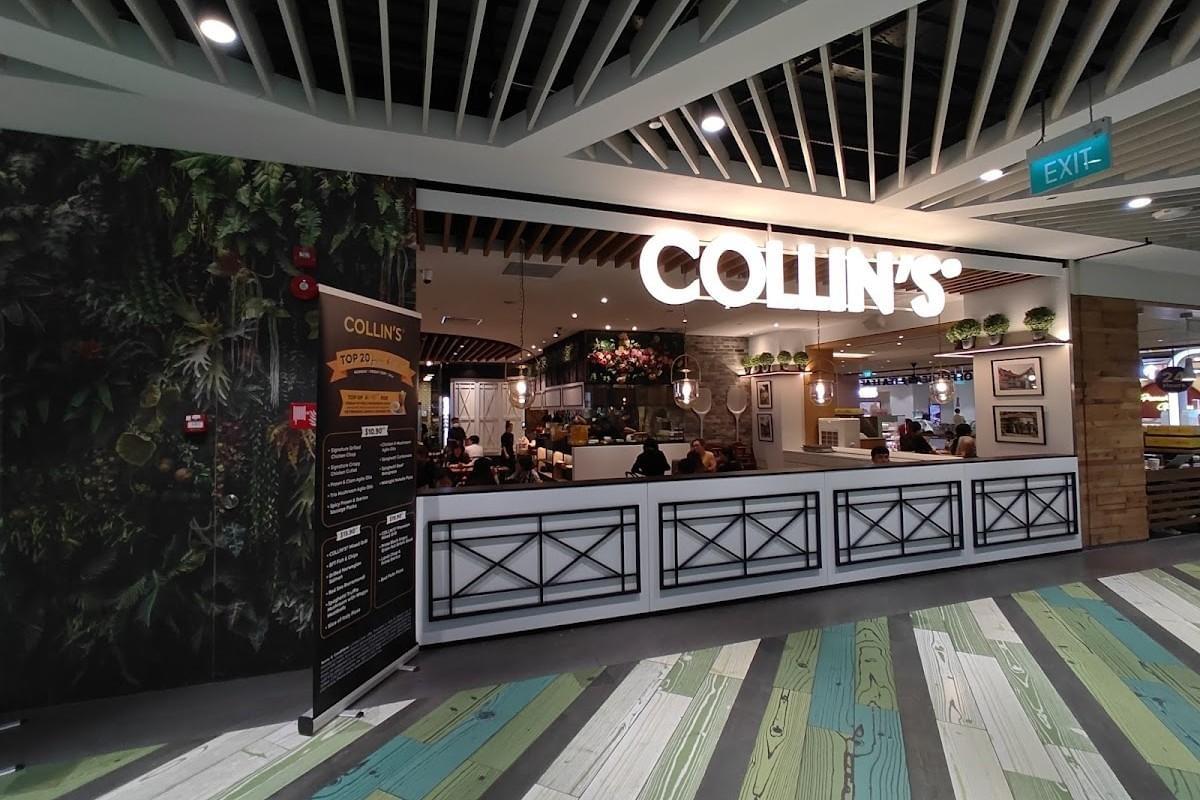 The facade of a COLLIN'S restaurant features a large, illuminated white sign above a modern dining area located inside a brightly lit shopping mall corridor. To the left, a tall black banner displays the menu next to a wall covered in a lush, green plant mural.