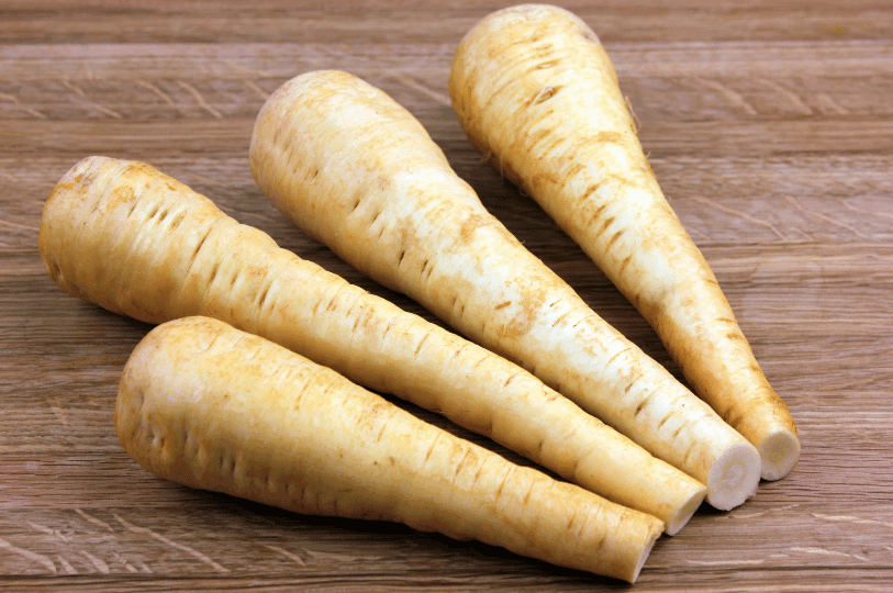 A batch of parsnips cut into uniform batons, tossed in oil and herbs, spread out on a metal baking sheet ready for roasting.