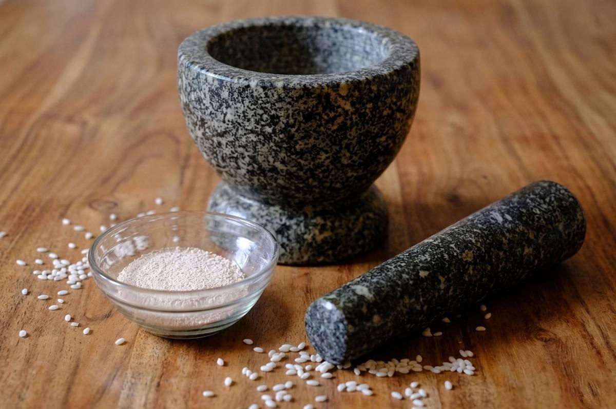 A stone mortar and pestle with toasted rice powder (khao khua) and raw rice, a crucial seasoning for Laotian Larb