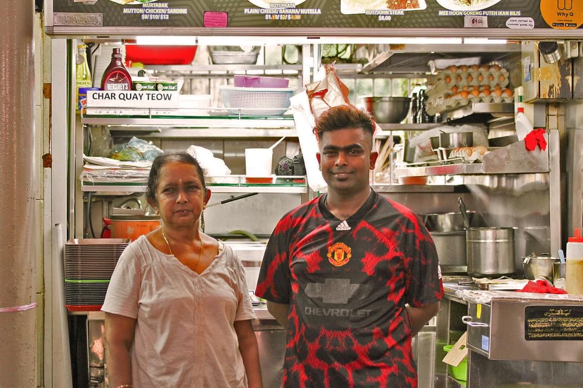 A pair of man and woman standing happily in front of a food stall with cutlery behind them