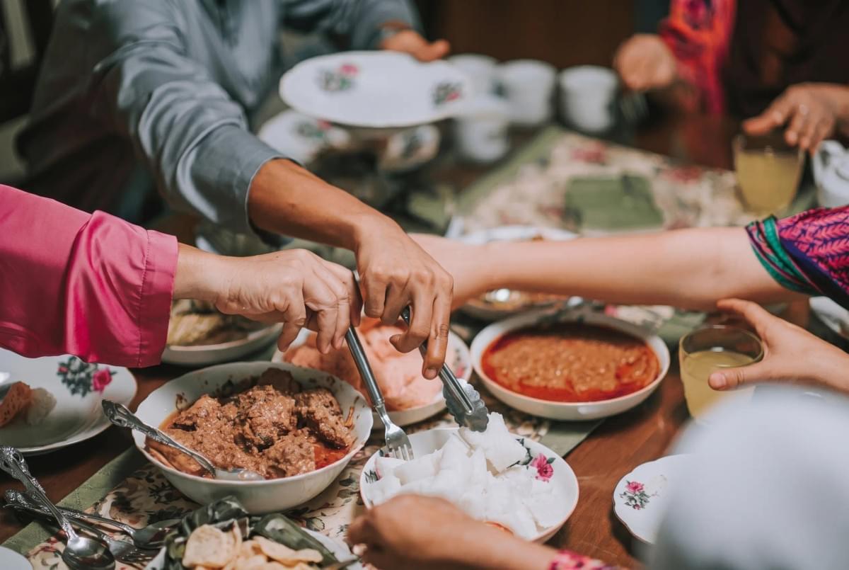 Group sharing a traditional feast of meat dishes, rice cakes, and sides around a dining table.