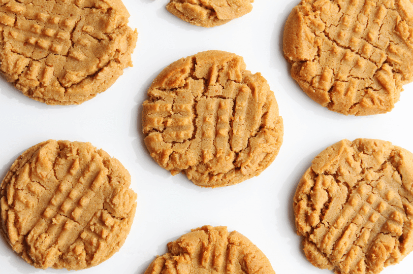 A high-angle view of freshly baked flourless peanut butter cookies arranged on a cooling rack, featuring a rich tan color and perfectly crisp edges.