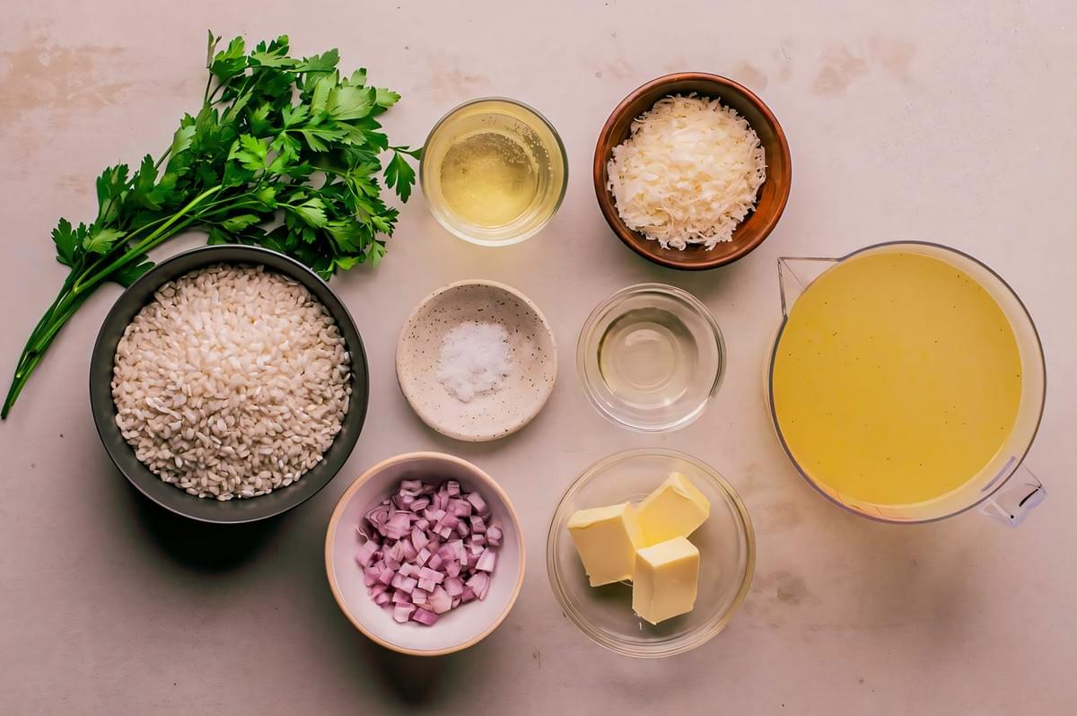 Flat-lay of risotto ingredients including arborio rice, broth, butter, onions, parsley, cheese, and white wine.