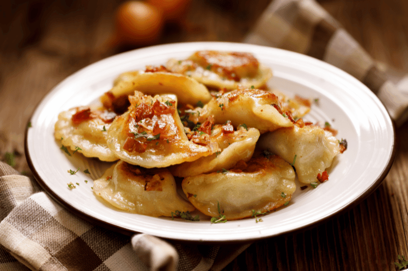 A plate of pan-fried golden-brown pierogi topped with crispy fried onions and fresh herbs, representing a savory traditional preparation.