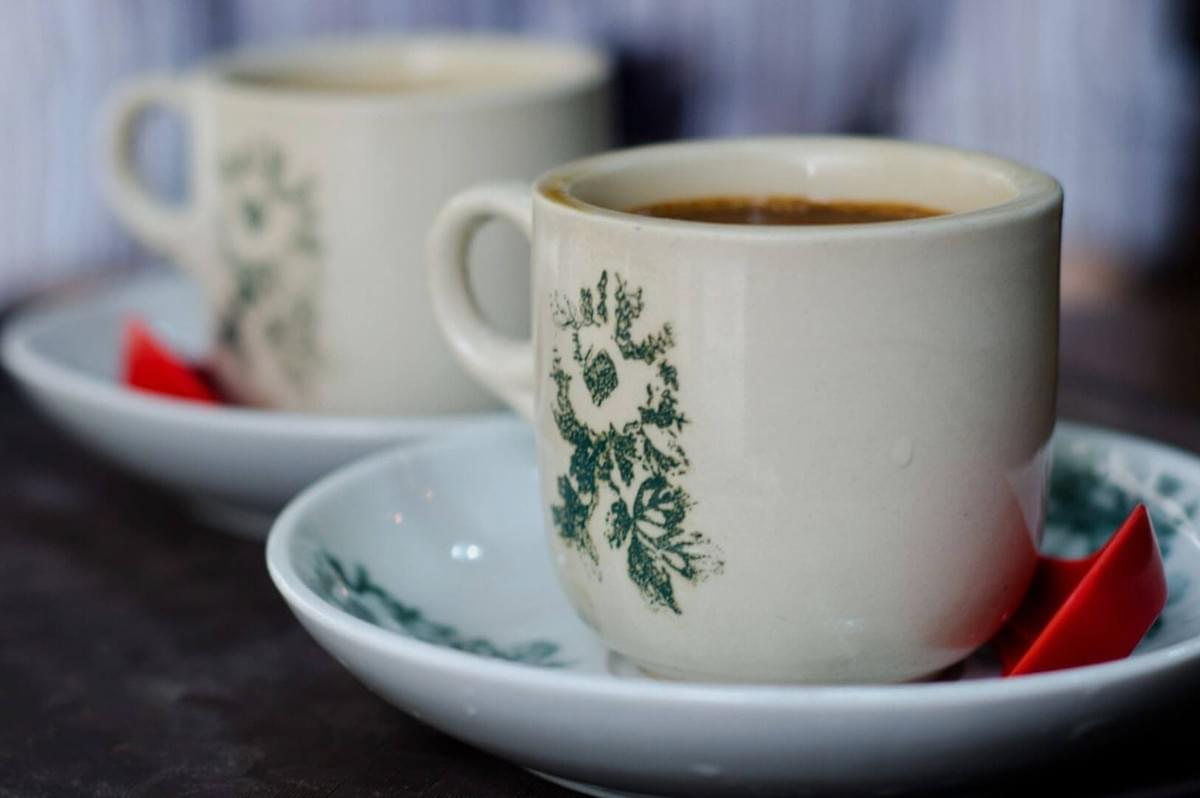 A close-up of two ceramic cups with green floral designs, filled with coffee on saucers. One cup is in focus, creating a warm, cozy atmosphere.