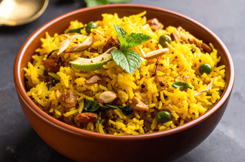 Close-up of vibrant yellow rice pulao served in a brown bowl, elegantly garnished with slivered almonds, fresh mint leaves, and a slice of lime.