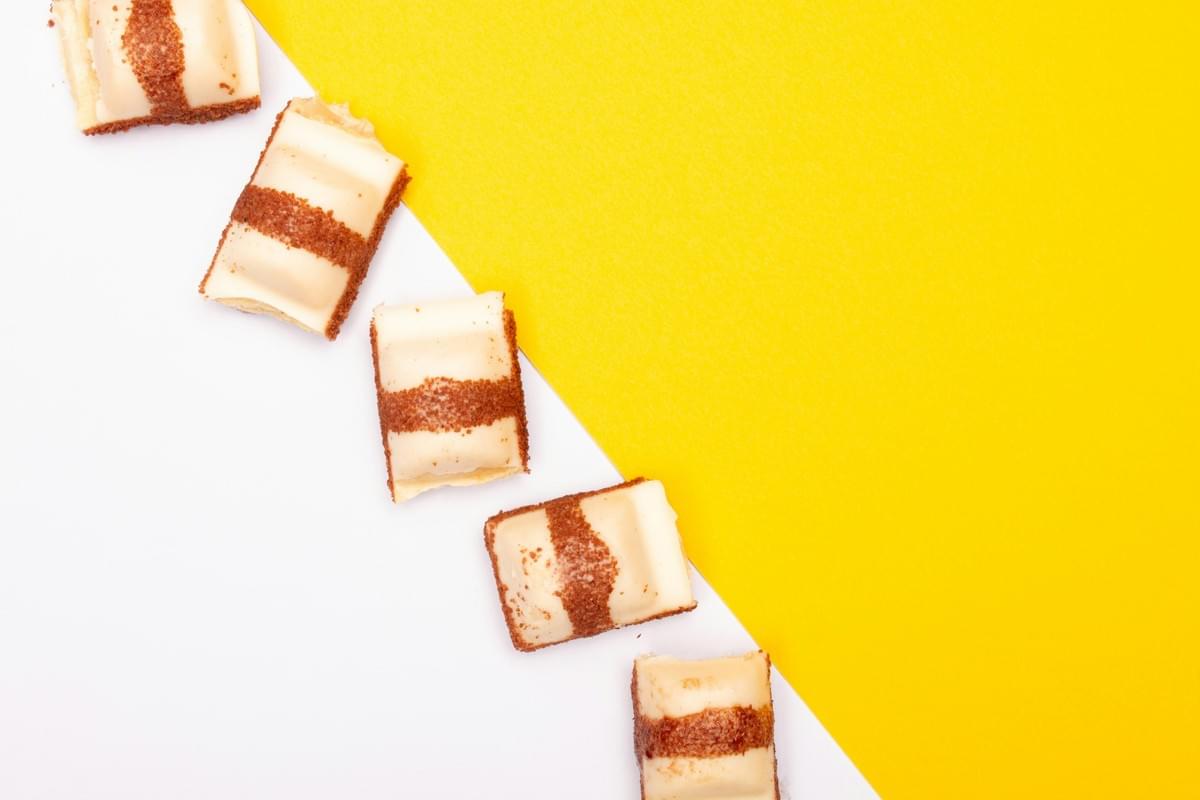 Five pieces of white chocolate Kinder Bueno bars are arranged diagonally across a split background. The background is divided sharply into solid white on the left and bright yellow on the right.