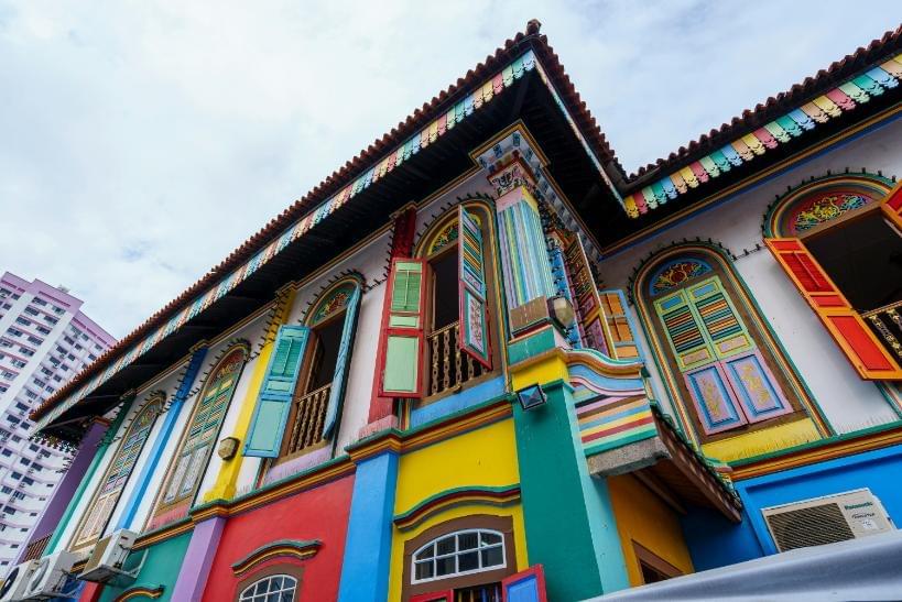 This image features a vibrant, low-angle view of a traditional two-story building known as the House of Tan Teng Niah, characterized by its dazzling array of rainbow-colored walls, intricate architectural details, and bright open shutters.