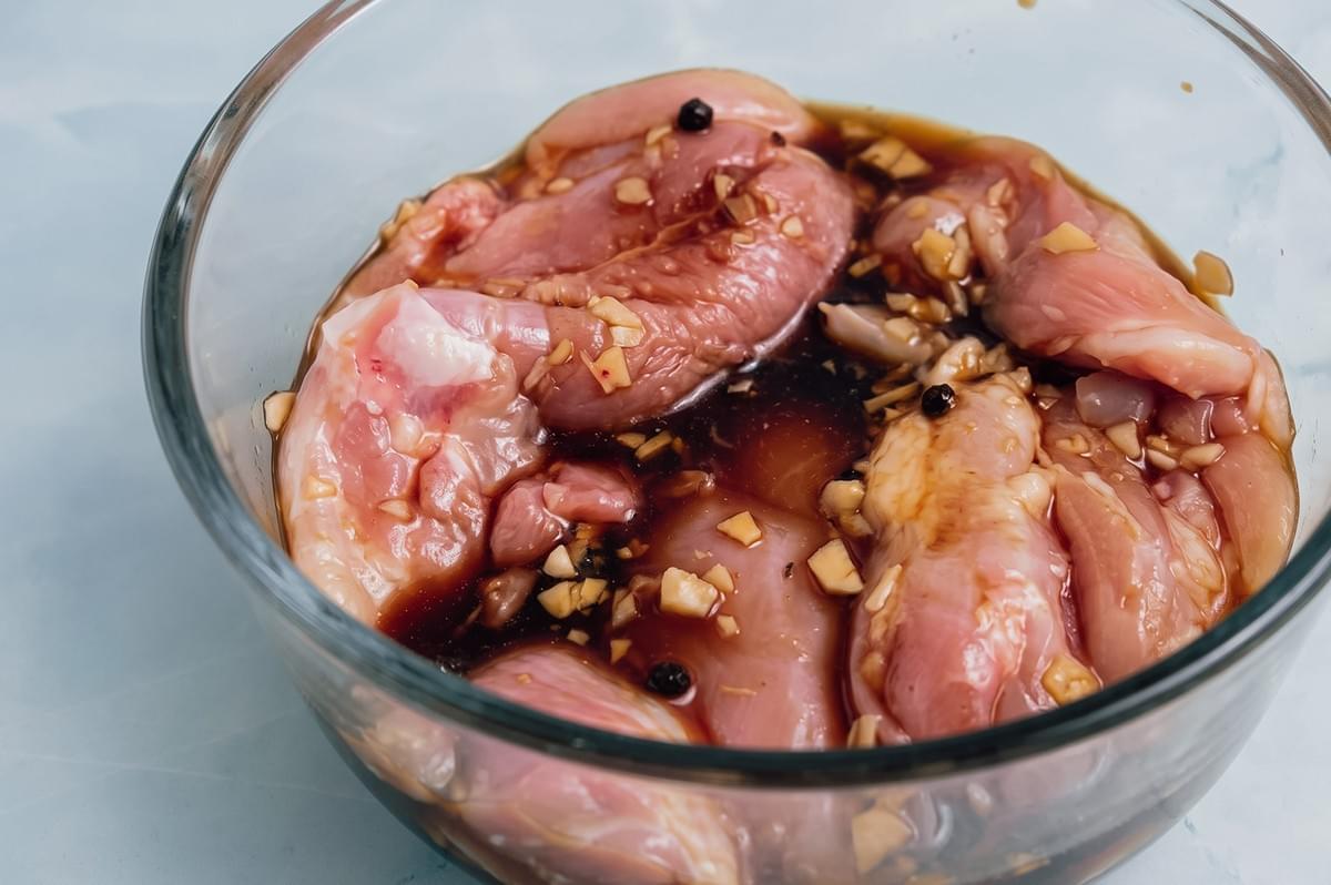 Slight overhead close-up of raw chicken marinating in soy sauce, garlic, vinegar, and peppercorns, the essential ingredients for an authentic Filipino chicken adobo recipe.