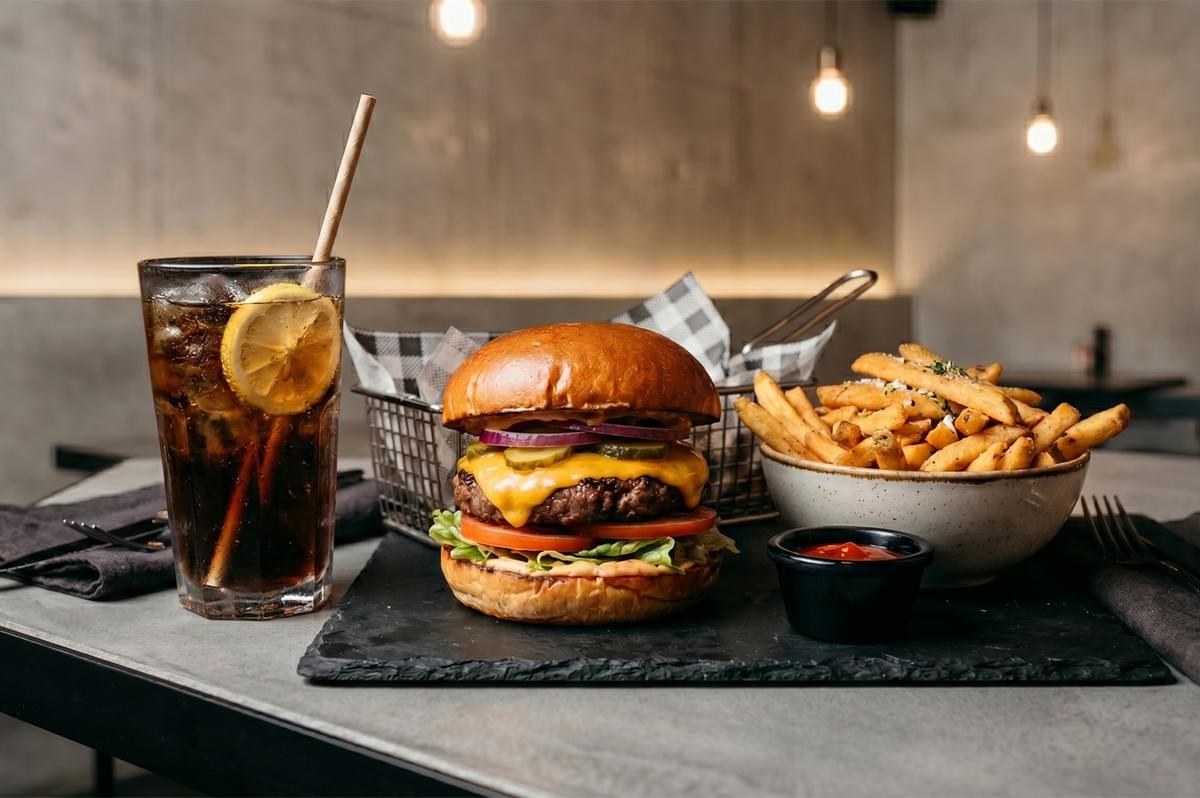 Cheeseburger combo meal with seasoned french fries and an iced cola drink on a restaurant table.