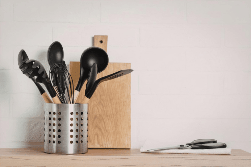 Kitchen shears resting on a paper towel next to a wooden cutting board and a metal utensil holder filled with various cooking tools.