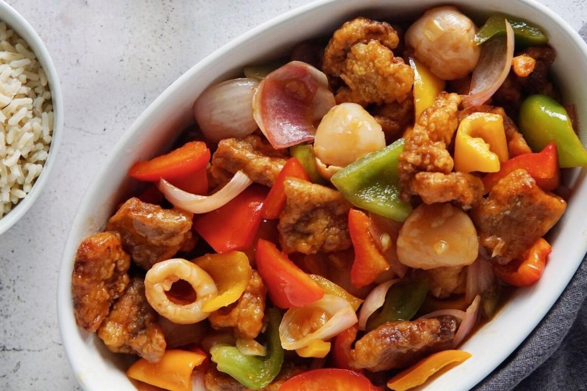 The image shows a vibrant bowl of crispy pork nuggets tossed with colorful bell peppers and onions in a glossy sauce. A side of steamed rice completes the meal, making for a classic and appetizing presentation.