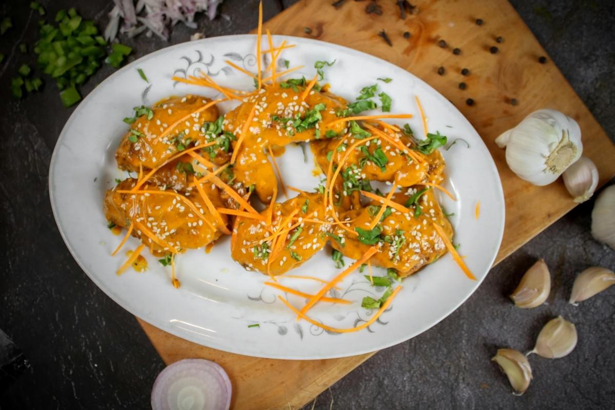 A wooden tray holds a pile of raw, cubed beef seasoned with pepper and heavily marbled with white fat. The dish is garnished with a sprig of green parsley and a small purple flower.