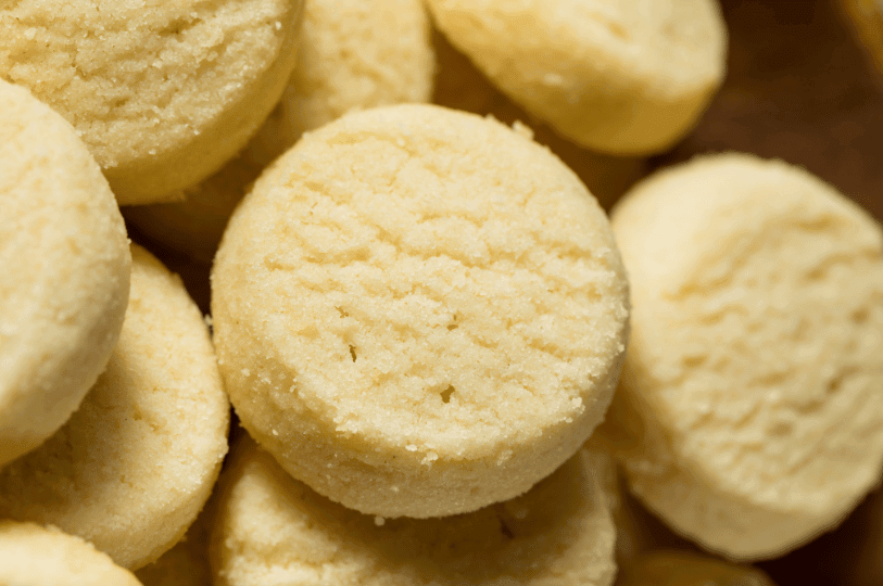 An extreme macro shot of a round shortbread cookie, showcasing the fine, sugary crystalline surface and the characteristic "short" crumbly break of the dough.