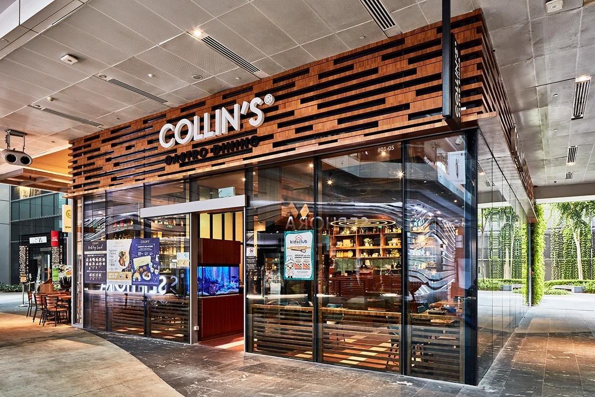 The image shows the modern storefront of "COLLIN'S GASTRO DINING," featuring a prominent slatted wooden facade above large, floor-to-ceiling glass windows. The brightly lit interior reveals indoor seating, shelves, and a prominent fish tank near the open entrance.