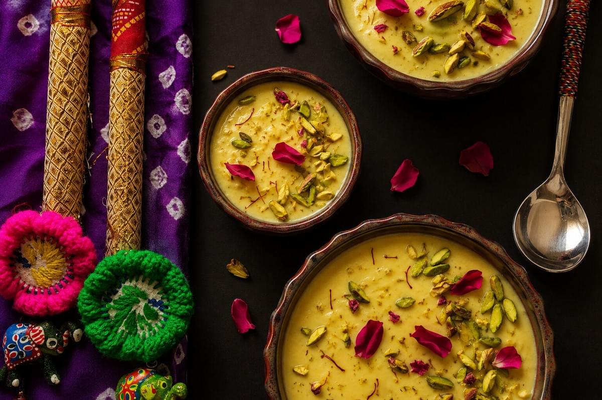 Top-down view of bowls of kheer garnished with pistachios and rose petals next to colorful festive decor.