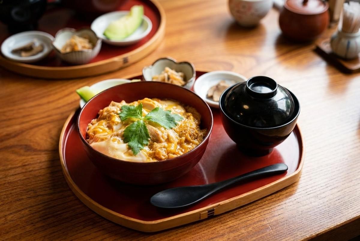 Traditional oyakodon chicken and egg rice bowl set served on a red lacquered tray. 