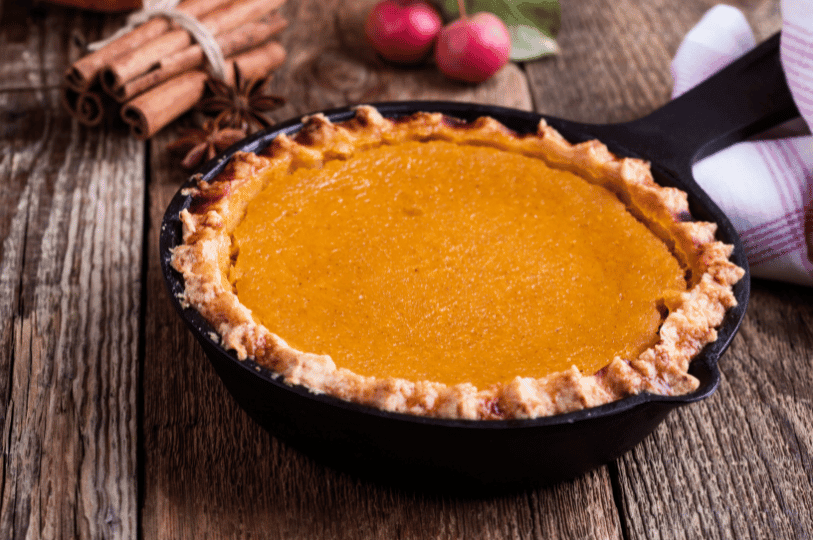 Golden pumpkin pie in a cast iron skillet, surrounded by cinnamon sticks, star anise, and apples—evoking cozy autumn flavors beyond tradition.
