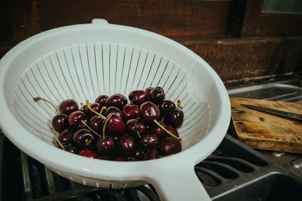 Fresh cherries in a white colander ready for washing in a kitchen sink