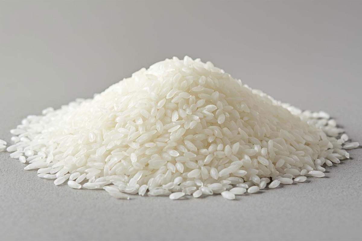 Close-up of a large mound of uncooked, white short-grain rice piled on a gray surface, highlighting the plump, opaque kernels.