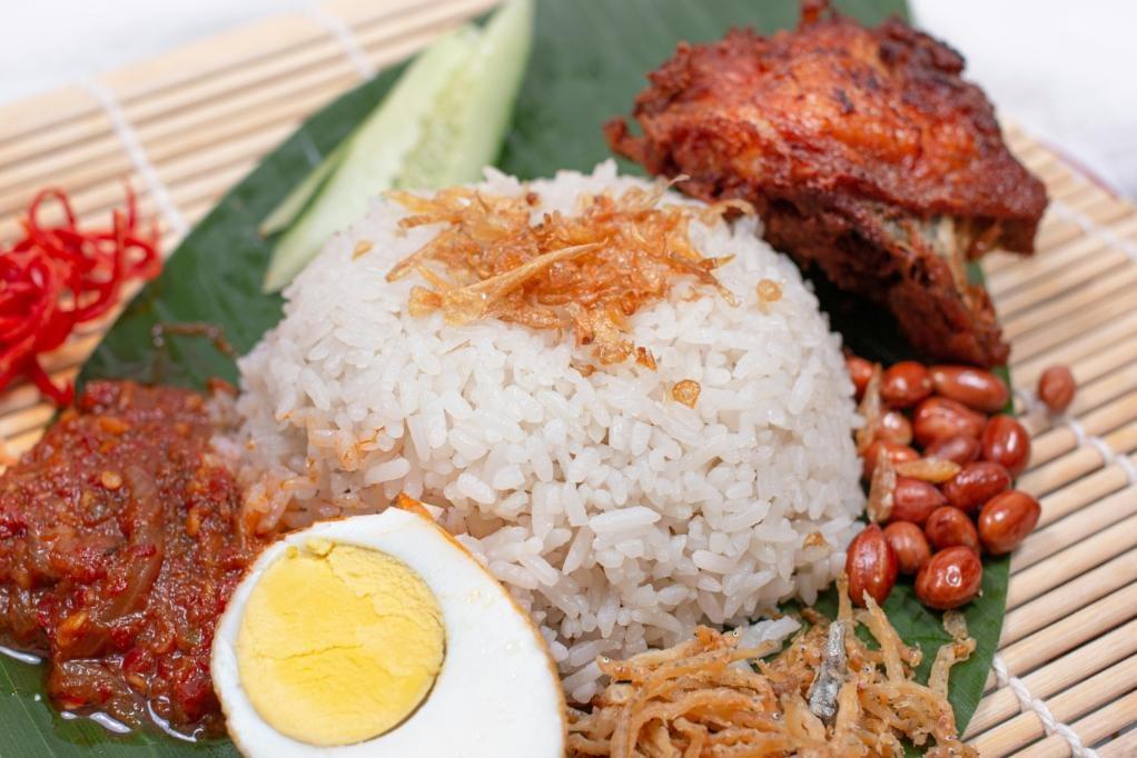 A close-up image of Nasi Lemak, a rice delicacy laid on top of a banana leaf over a bamboo matting.