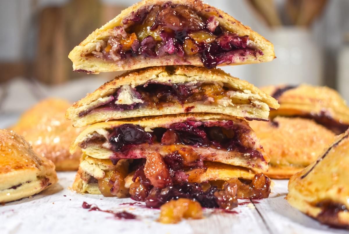 Stack of baked hand pies cut in half to show a rich blueberry and peach fruit filling.