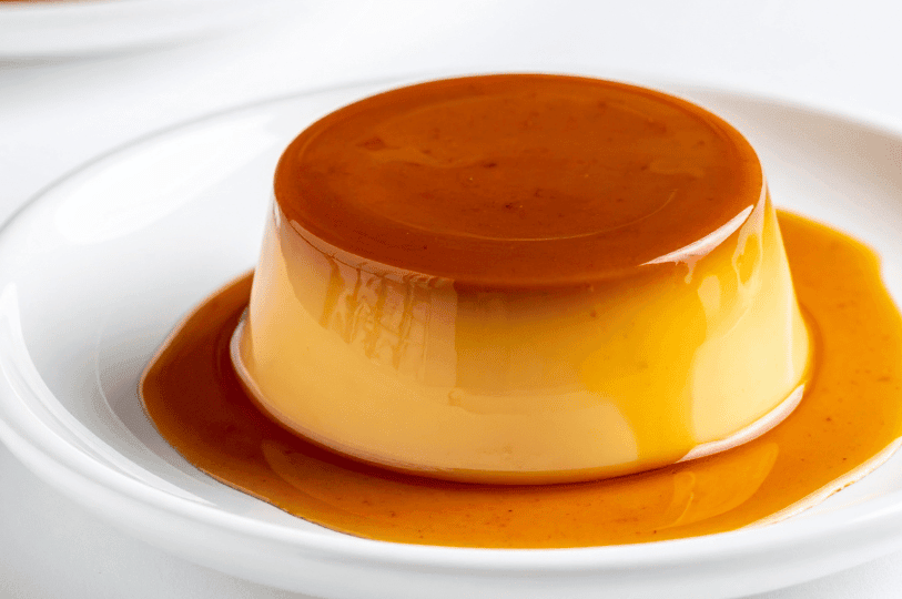A perfectly smooth, circular flan centered on a white plate, highlighting its clean edges and the translucent layer of liquid caramel at the base.