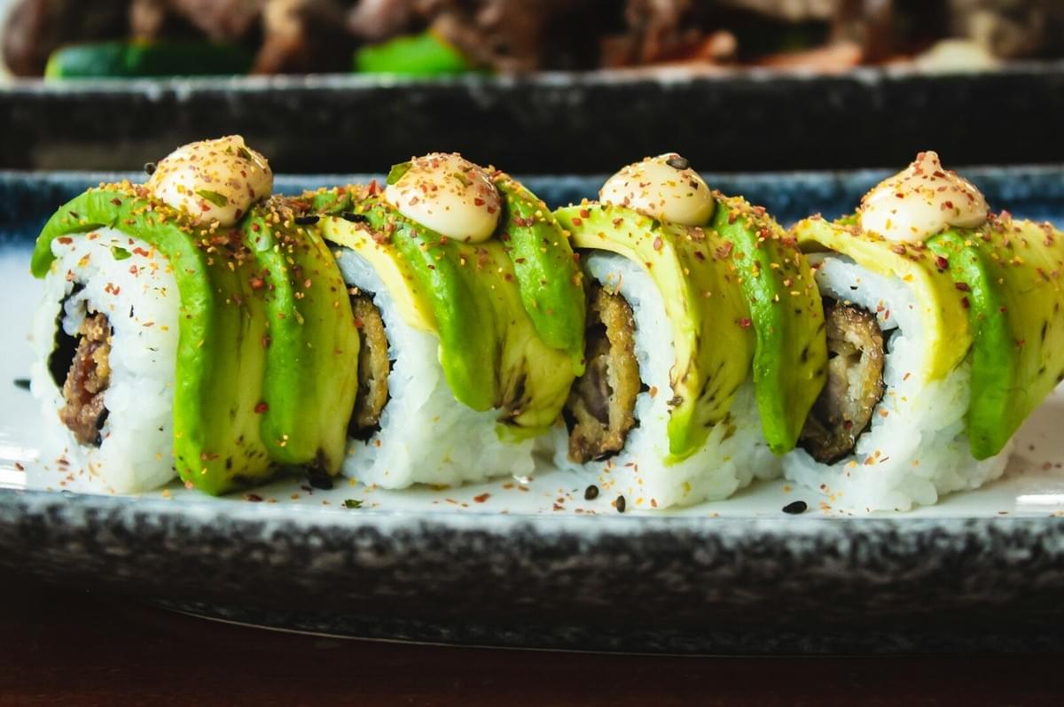 A vibrant sushi roll with avocado and assorted fillings, presented at a Japanese Vegan Izakaya.