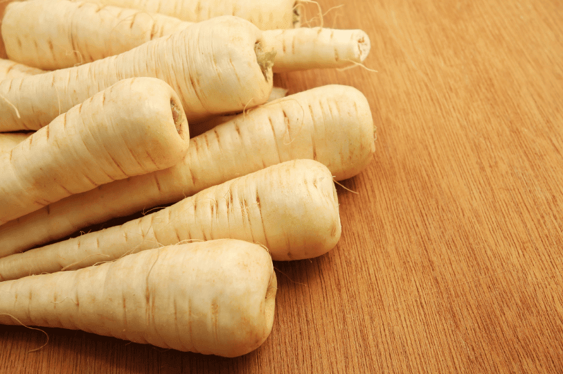 A close-up of parsnips being peeled, showing the transition from the rough, tan outer skin to the crisp, cream-colored flesh inside.