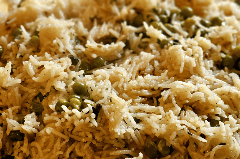 A macro texture shot of fluffy, long-grain rice pilaf mixed with green peas and toasted cumin seeds.