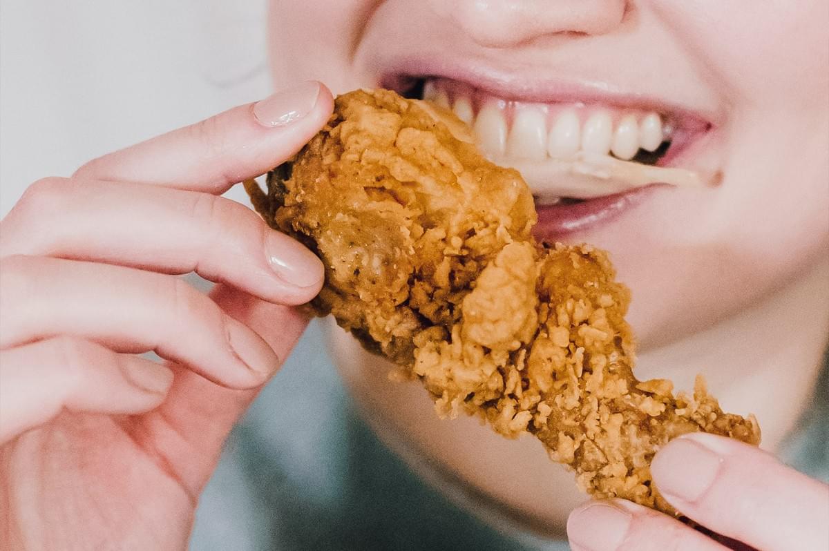 Close-up macro shot of person eating fried chicken showing emotional eating behavior and cravings for high-fat comfort food during stress abroad