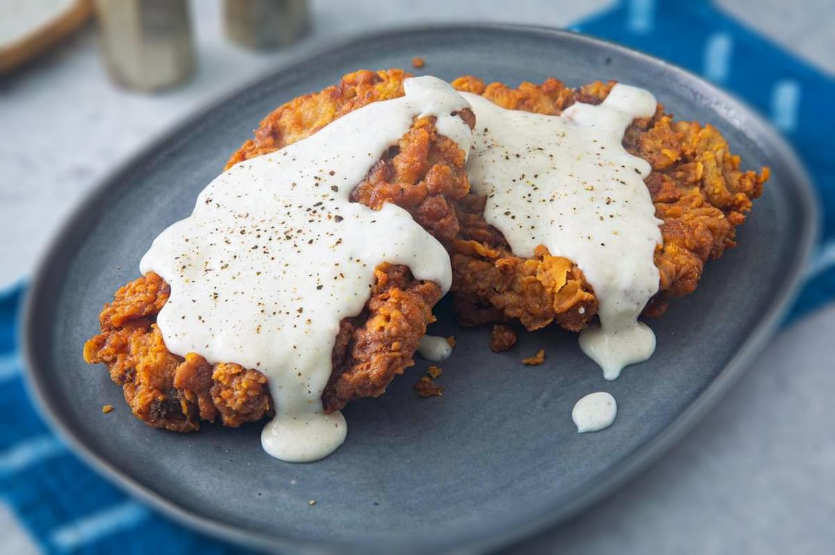 Southern chicken-fried steak topped with creamy country gravy on a gray plate.