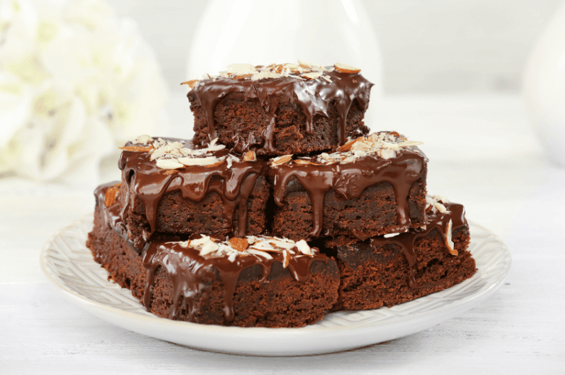 A pyramid of glossy chocolate brownies topped with sliced almonds, styled for an elegant, fudgy-texture presentation.