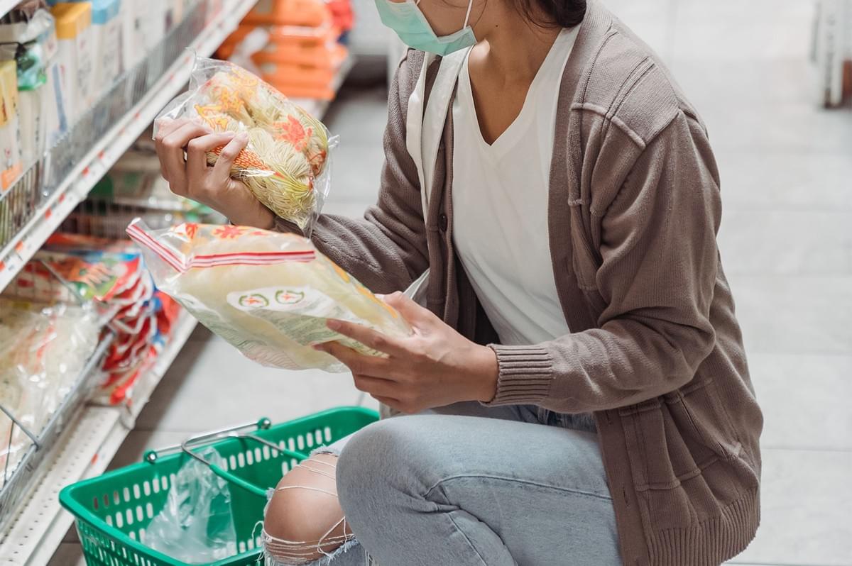 Woman reading food labels and checking halal products in a supermarket aisle.