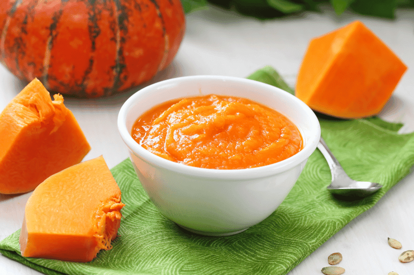 Bright orange pumpkin puree in a white bowl, surrounded by raw pumpkin slices and scattered seeds—celebrating autumn’s versatility from field to kitchen.