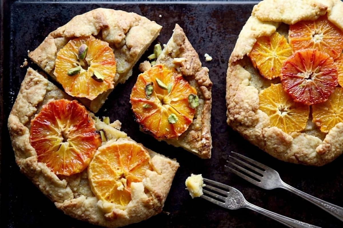 Citrus galettes with blood orange and orange slices topped with pistachios on dark baking sheet