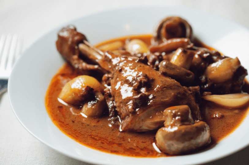 An elegant individual serving of Coq au Vin on a white plate, highlighting the deep burgundy color of the traditional French sauce.